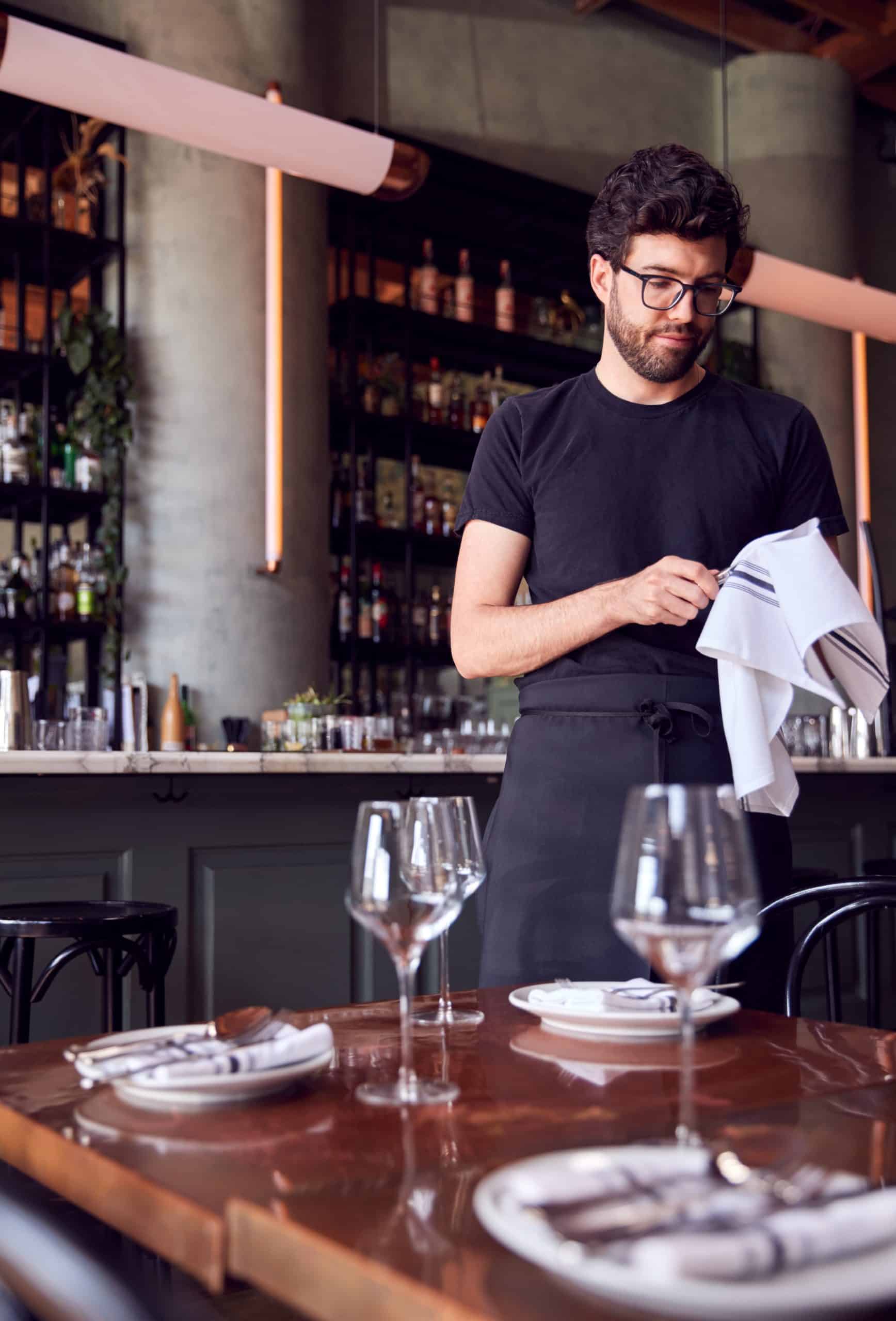 Male Waiter Polishing Glasses Before Service In Bar Restaurant